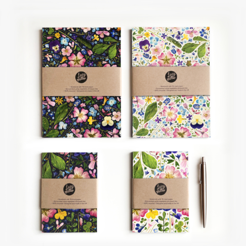 Four pressed flower notebooks on a white background. Each notebook is secured with a kraft belly band. There are two A6 and two A5 notebooks.