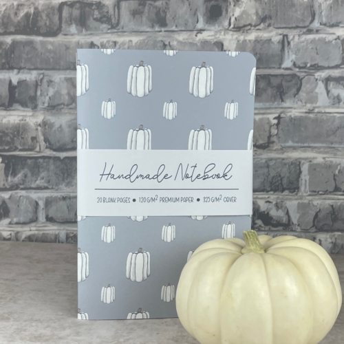 Handmade notebook with hand drawn white pumpkins in two sizes in a vertical pattern on a light blue cover.