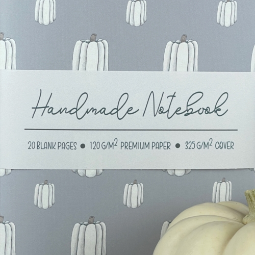 Close up of a handmade notebook with hand drawn white pumpkins in two sizes in a vertical pattern on a light blue cover.